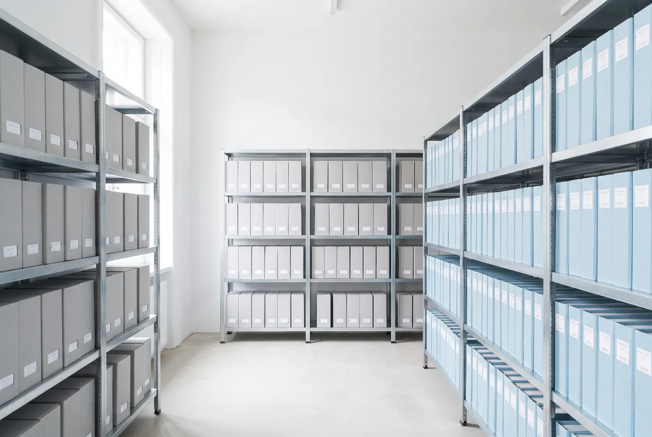 Shelf of pale document boxes and ledger spines in a bright records room