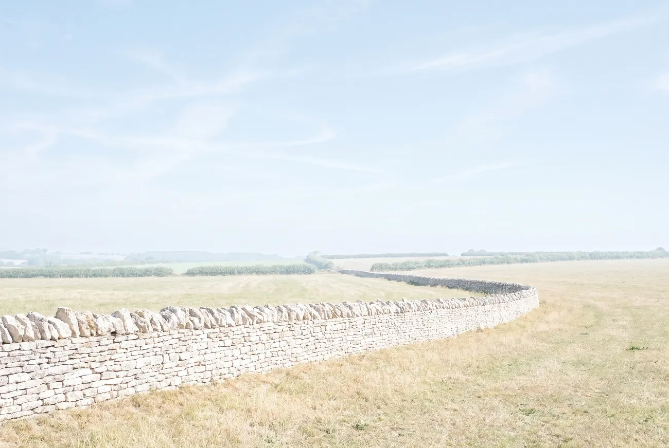 Dry-stone wall running across open farmland in clear light
