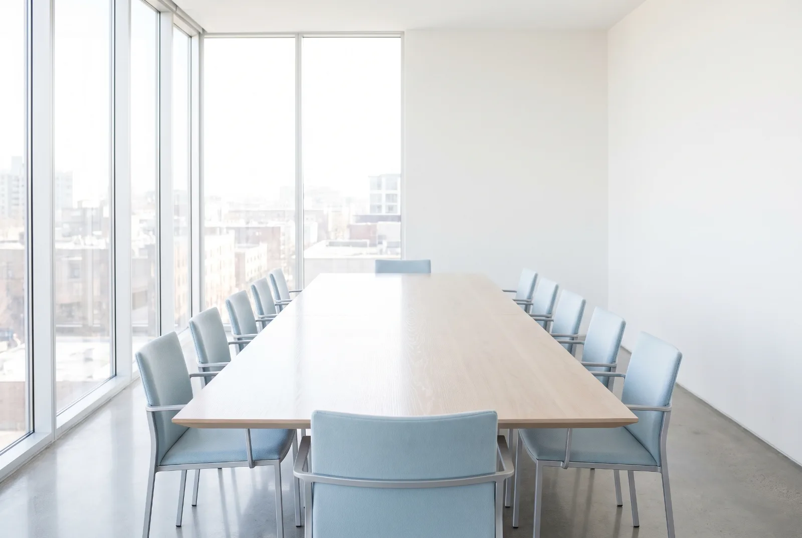 Empty meeting room with a long pale table and a wall of glazing
