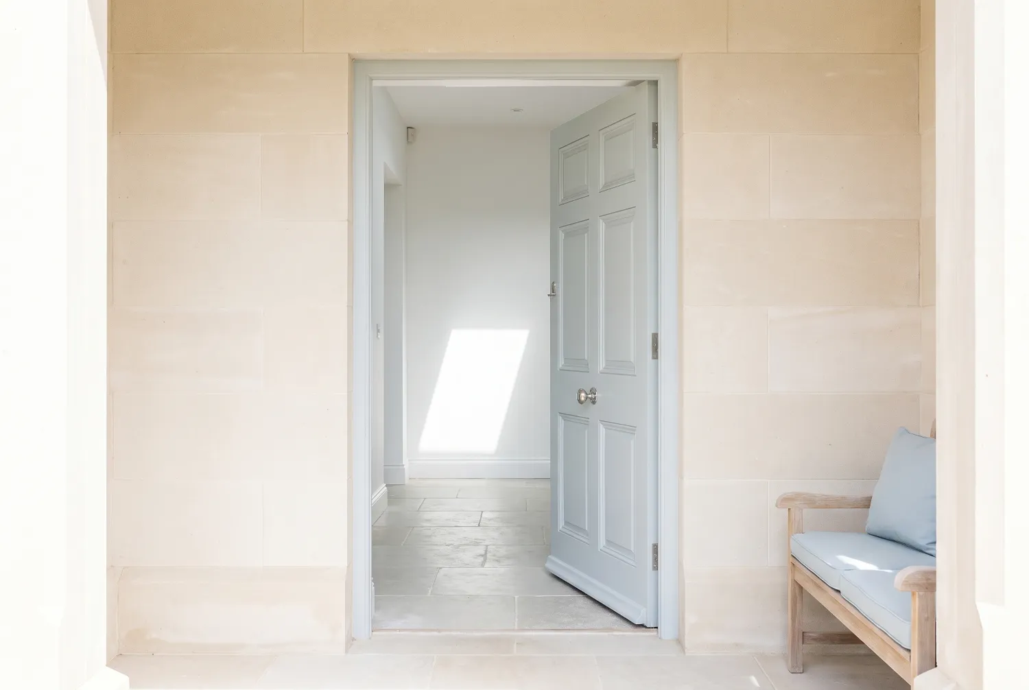 Stone porch with a panelled door standing half open onto a flagstone hallway